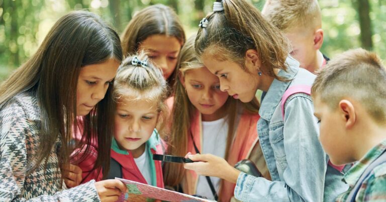 Un groupe de jeunes campeurs regarde avec enthousiasme une carte et une boussole travaillant ensemble au camp d’été.