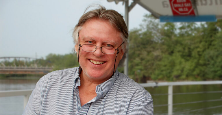 Jim Wilson sous un auvent sur le bord d’une rivière, souriant largement.