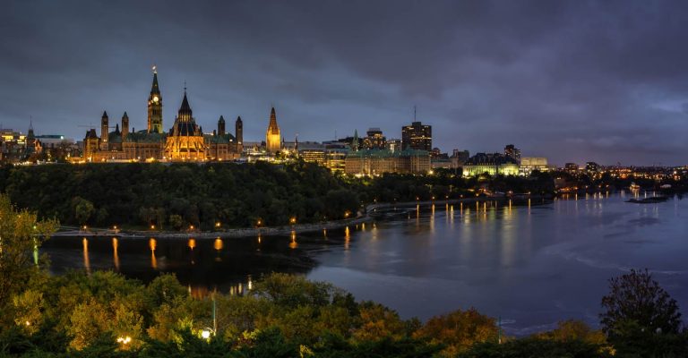 Vue des édifices du Parlement à Ottawa au-dessus de la rivière, la nuit, avec un ciel nuageux et maussade.