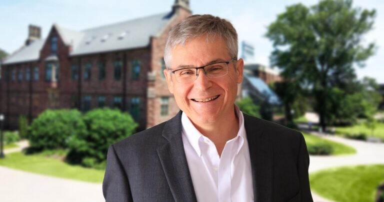 Le campus de Mount Allison s’étend en arrière-plan par une journée d’été, avec Mario Levesque souriant joyeusement au premier plan.